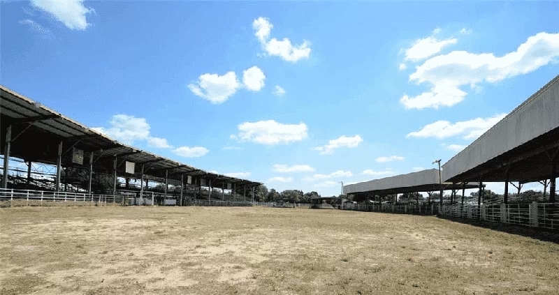 Large dirt field flanked by stables on either side.