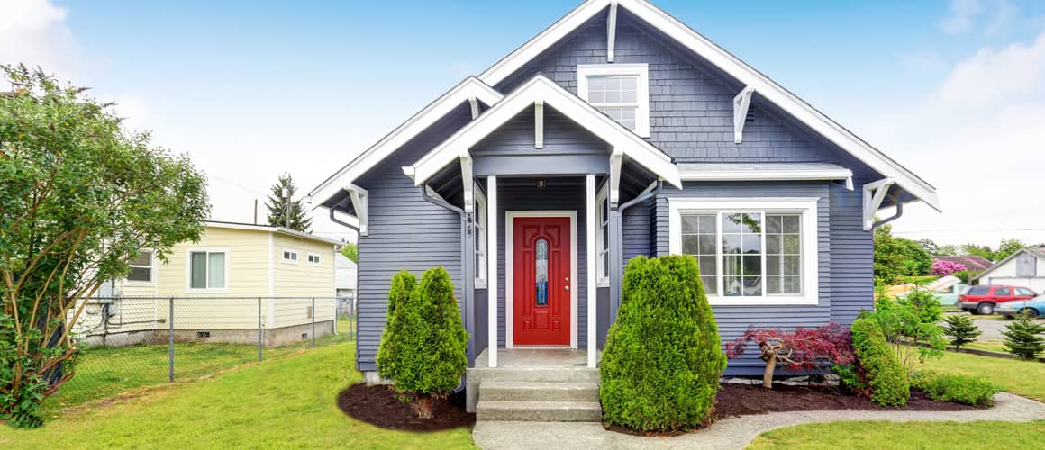 A small indigo colored house with a red door and green front yard.