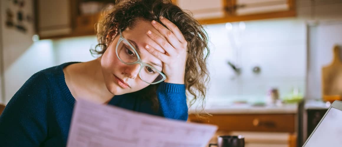 Woman looking over a bill in her kitchen.