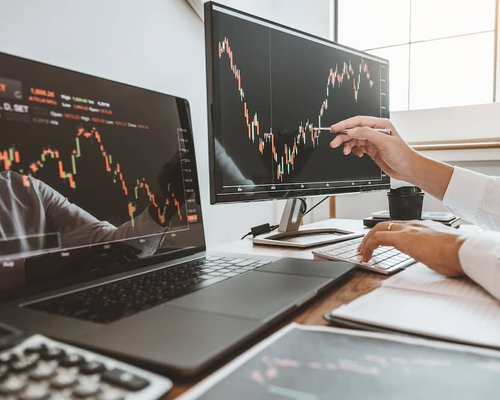 Person in front of computer monitors tracking stock charts.