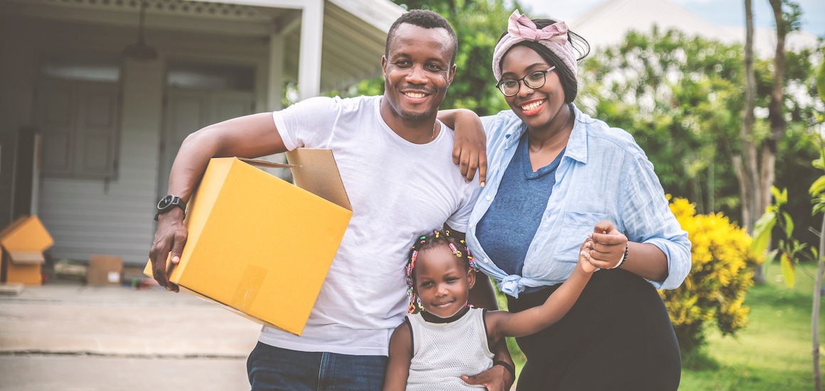 A family in the process of moving into a new home, carrying boxes and belongings.