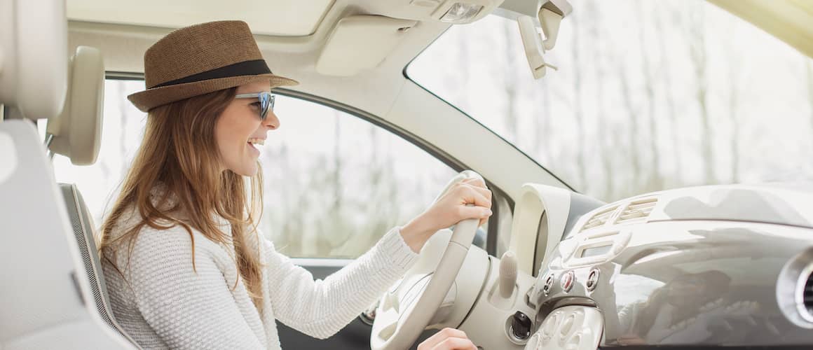 Woman wearing hat and sunglasses while driving new car.