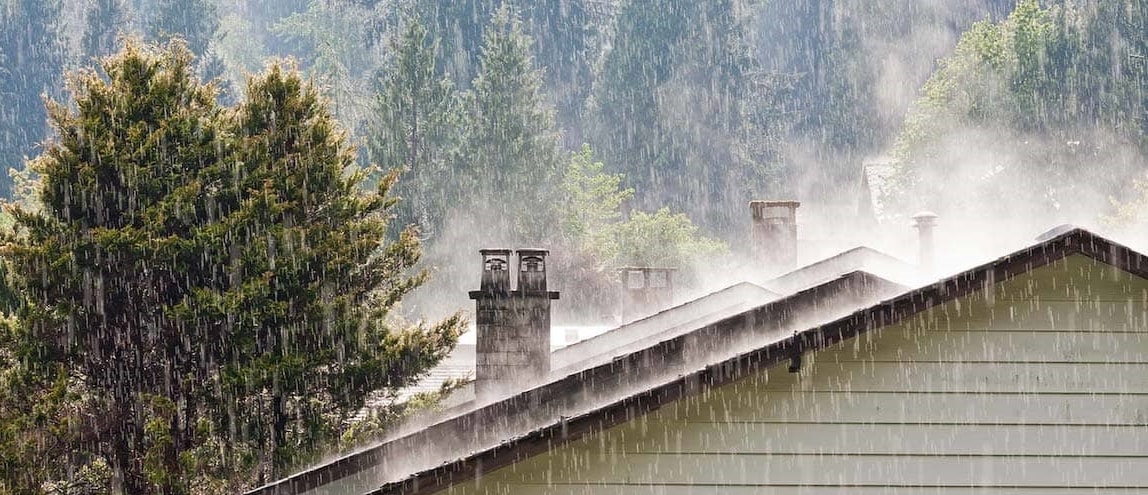 A house roof in woods under heavy rain, possibly symbolizing emergency plan for home during a natural disaster.