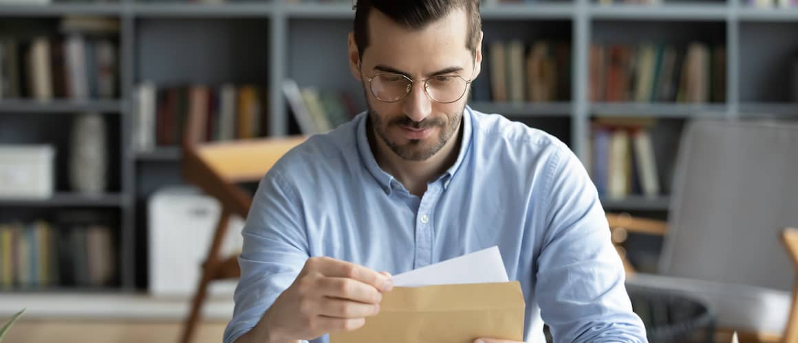 Man sitting at a desk and reading a letter in an envelope.