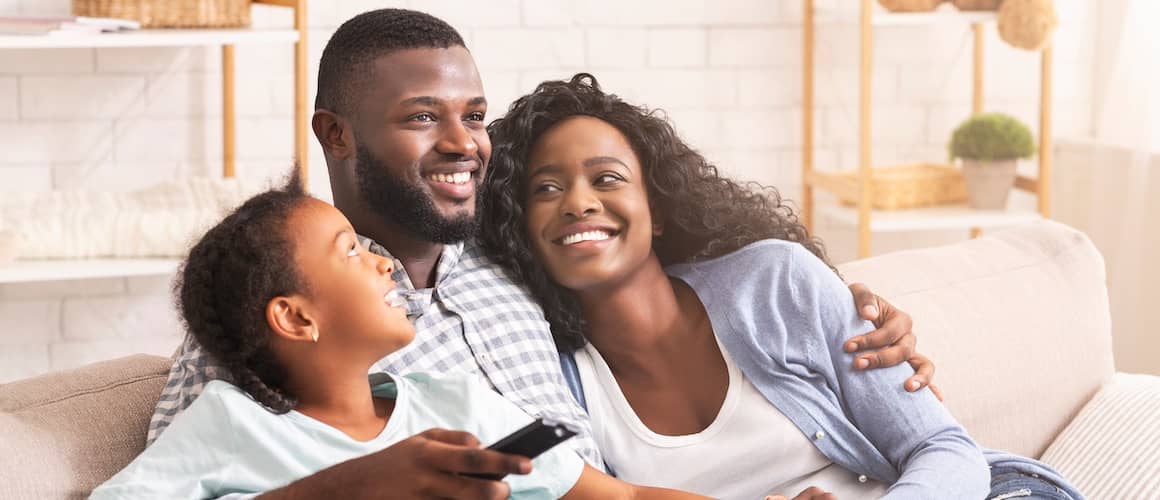 Family of three smiling together while sitting in a couch.