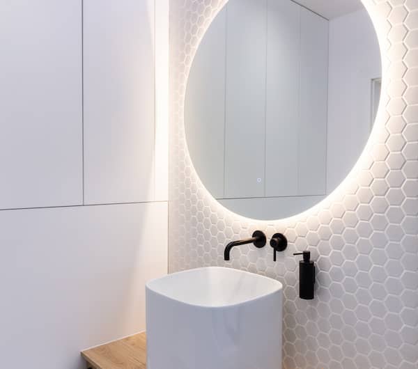 Small half bathroom with backlit mirror and interlocking hexagonal tiles on the wall.