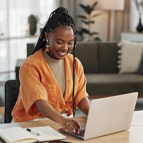 Woman in orange top typing on laptop.