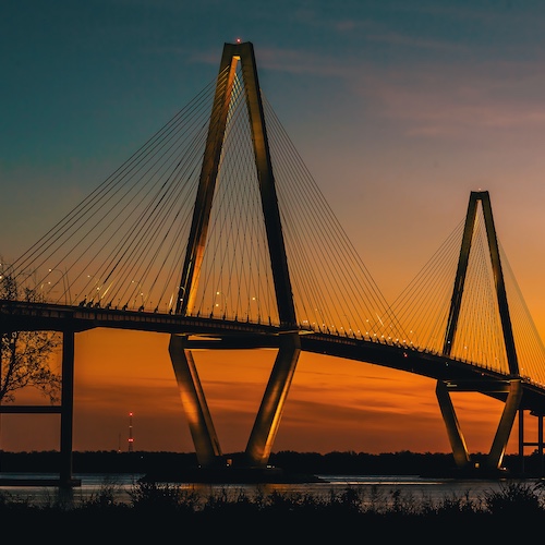 Large bridge located in South Carolina in front of a sunset lit sky.