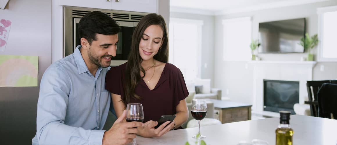 Image of man and woman looking down at phone in kitchen, smiling.