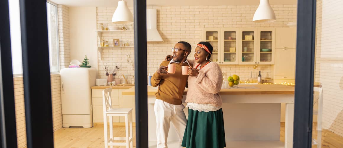 A couple having a beverage in the kitchen and looking outside the window.