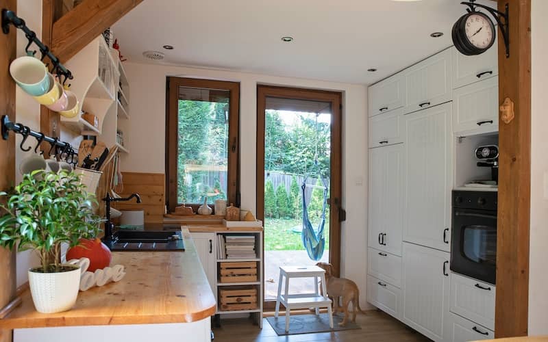 Quaint but modern cottage kitchen with built in cupboards, large glass door and window, and cutting board lined countertop.  