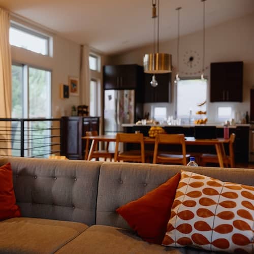 Couch with red pillows and kitchen out of focus in the background.