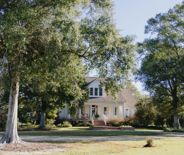 Mature trees surround a two-story home with an inviting porch and an expansive lawn.