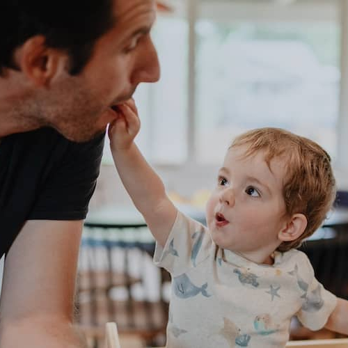 Father with young child eating together in kitchen.