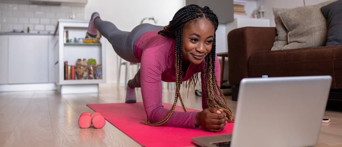 Woman on a pink yoga mat in living room in front of laptop.