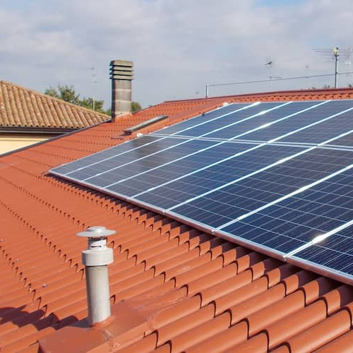 Line of solar panels on a red shingle roof.