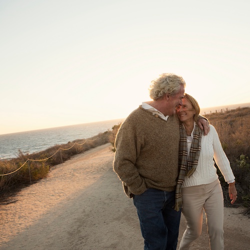 Older couple strolling together on Newport Beach at dusk.