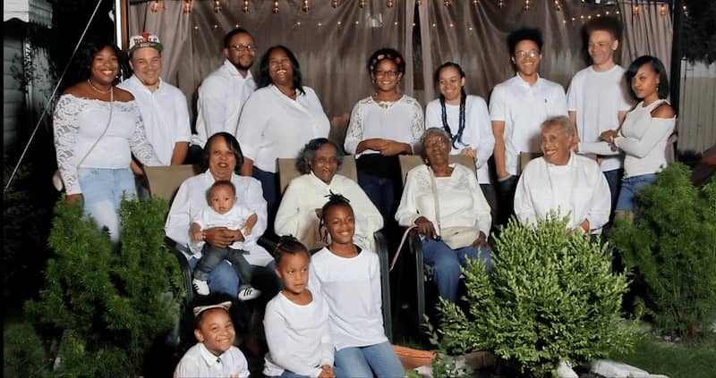 Large family stands in front of a beige backdrop, smiling.