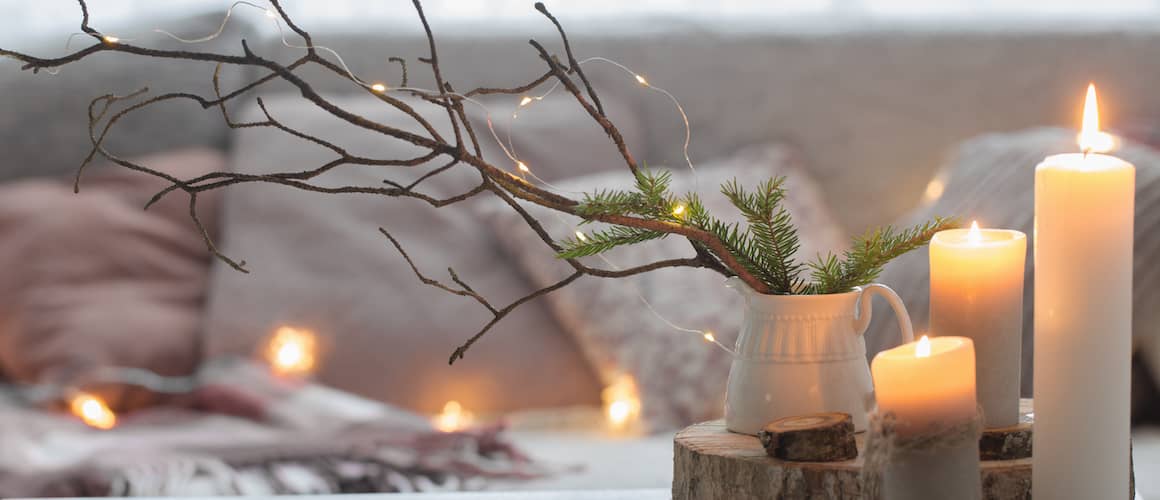 A coffee table set with candles and small pine branches.