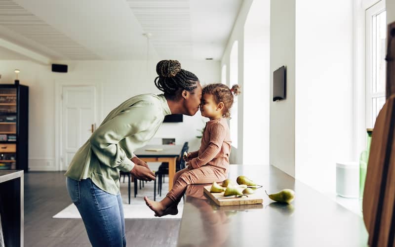 Mother and daughter in kitchen nuzzling noses and laughing.