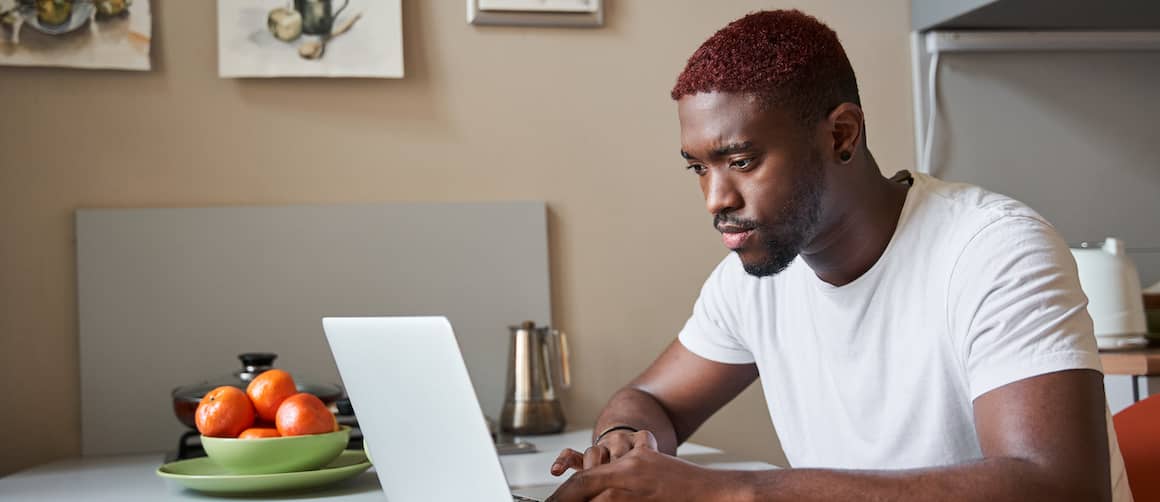 Young man at kitchen table working through his finances on laptop.