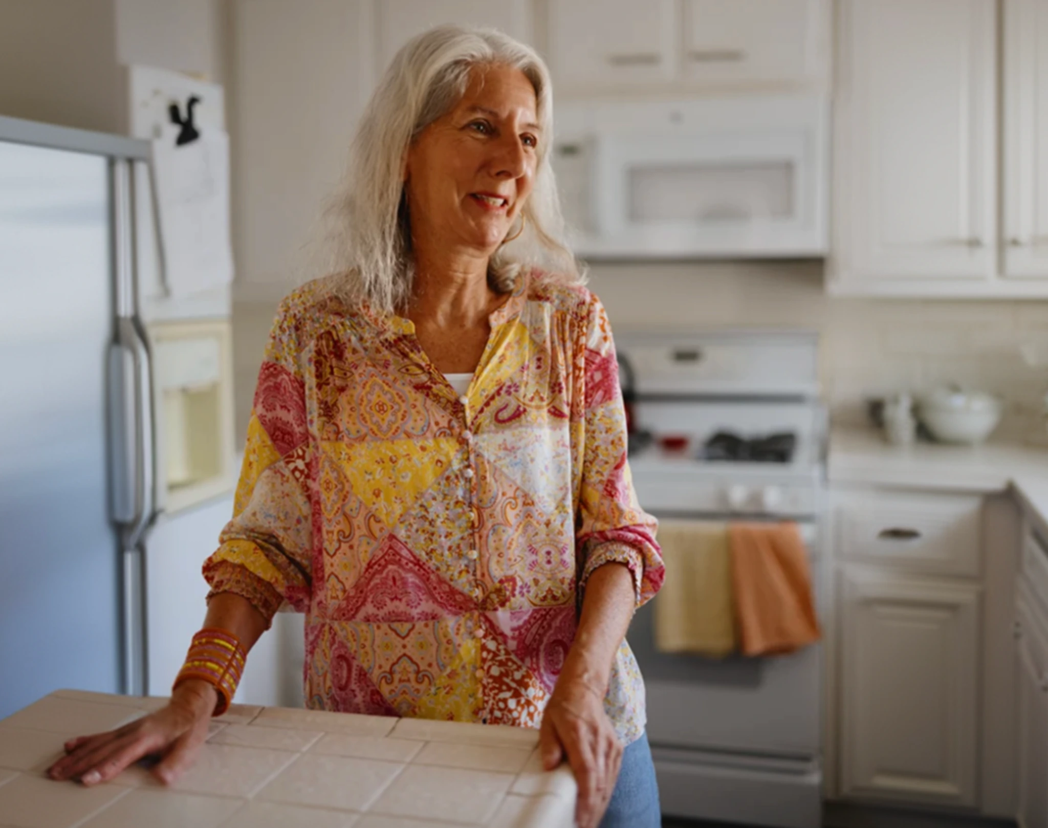 Older woman standing in a kitchen, smiling with hands resting on a countertop