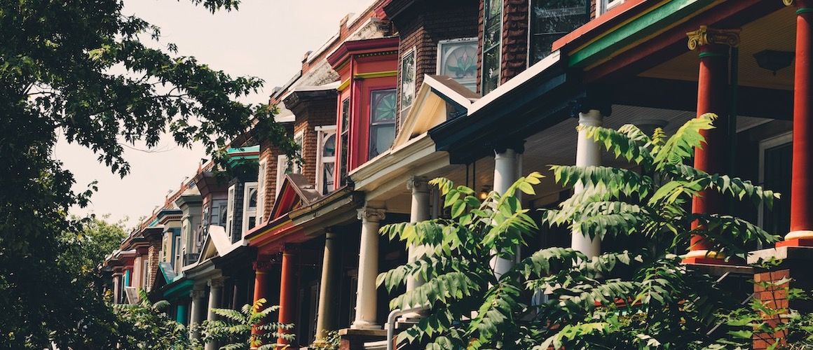 A row of colorful houses with foliage in the foreground blocking some of them from view.