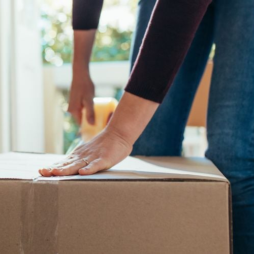 A woman sealing a box with tape, possibly indicating the process of moving or packing belongings for a new home.