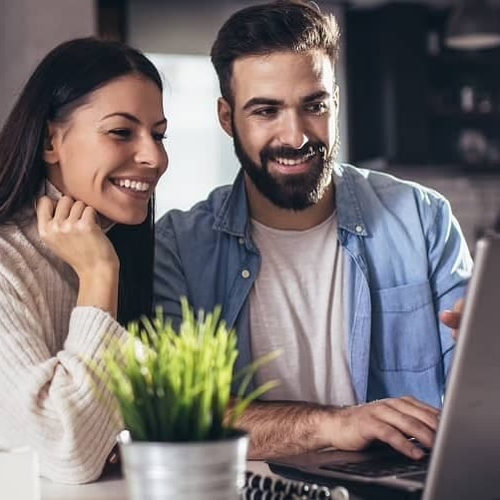 A couple engaged with a computer in their home, likely researching or managing aspects related to their property or residence.