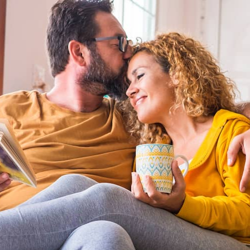 A happy couple reading and drinking coffee on a couch, likely depicting leisure or relaxation at home.