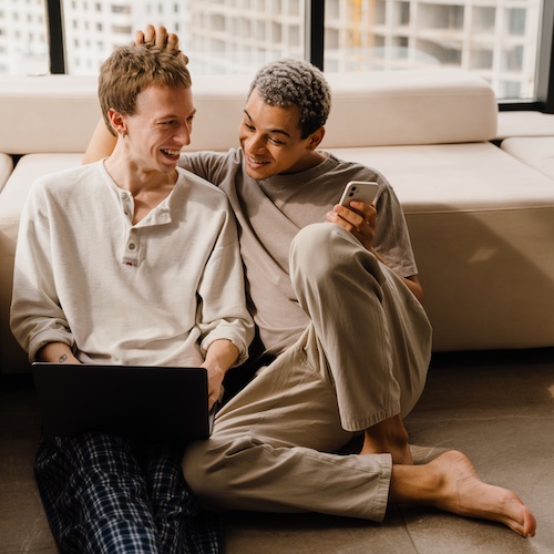 Couple sitting on the floor of their home side by side and smiling together.
