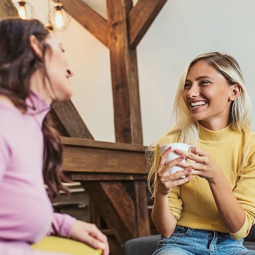 Two women in conversation while seated on a couch.
