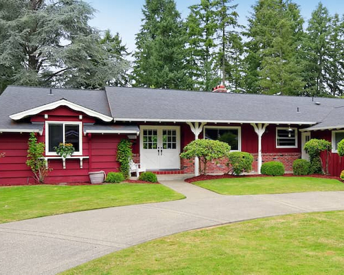 A red one-story home with a neatly trimmed lawn and trees, presenting a cozy residential scene.