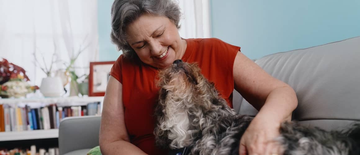 Woman snuggling fluffy dog on couch.