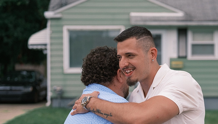 Man in white shirt hugging man in blue shirt.