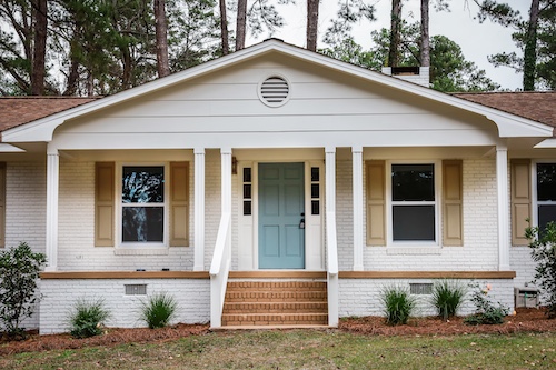 The front exterior entrance of a newly painted white siding brick ranch style house with a large yard that has been recently renovated.