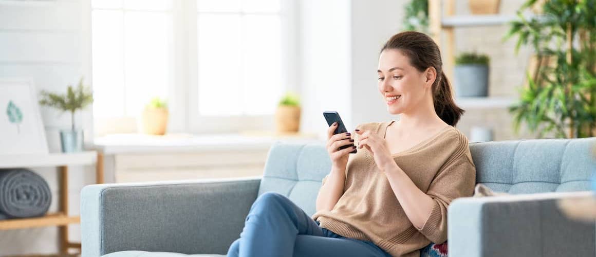 Woman sitting on her couch at home and using her cell phone.