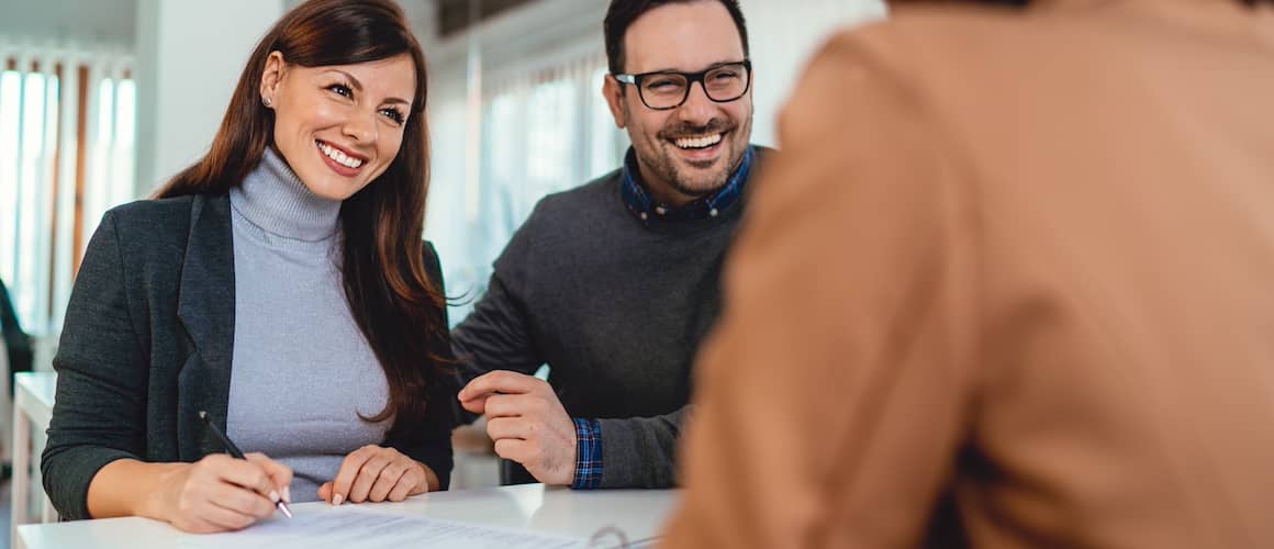 Couple at office with banker signing documents and smiling.