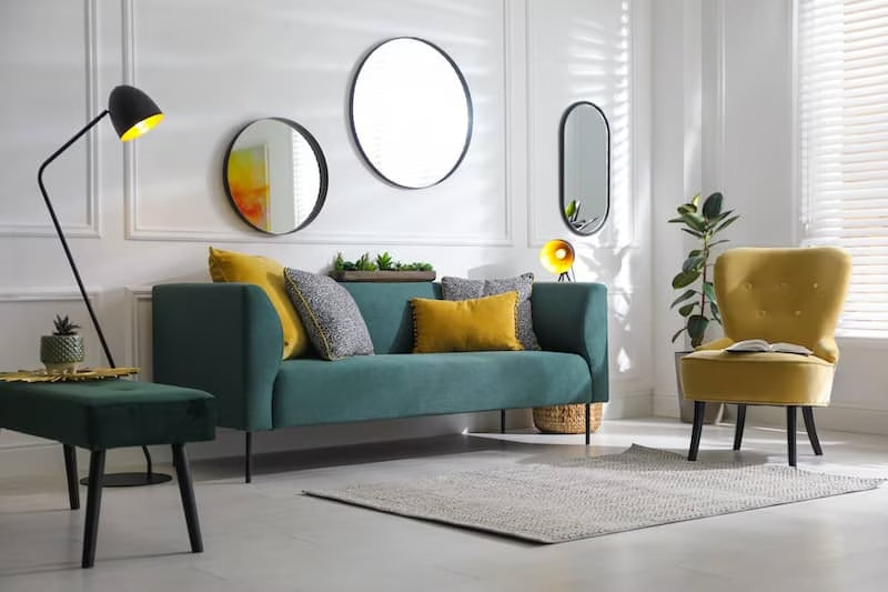 Contemporary living room with various mirrors on wall and velvet couch and side chair.