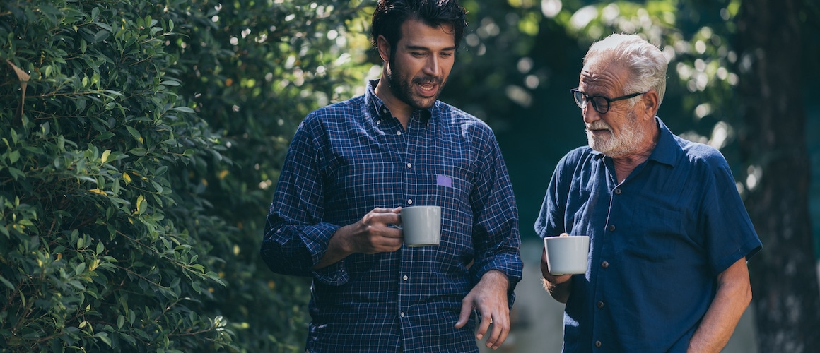 Adult son and senior father talking with a cup in their hands, suggesting family or generational bonding.