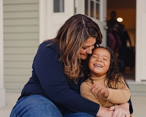 Woman holding daughter while sitting on porch smiling.