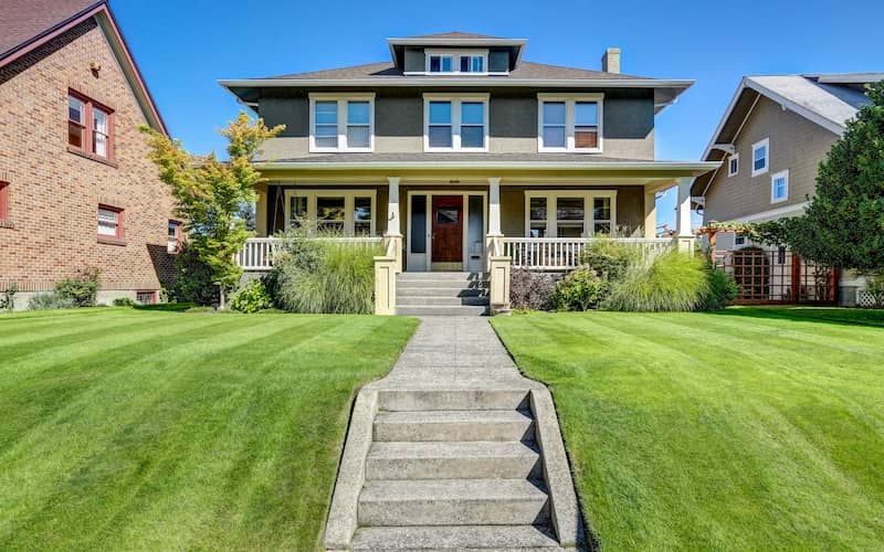 Four-square craftsman-style home with large covered porch and manicured lawn. 