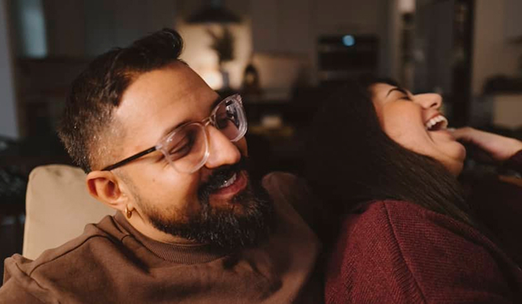 A man and woman sit on the living room floor, laughing.