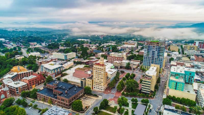 RHB Assets From IGX: Scenic view of downtown Asheville, North Carolina surrounded by lush greenery and mountains.