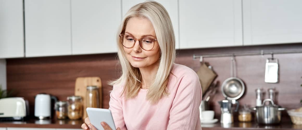 Woman looking pleased while doing business on smartphone in kitchen.