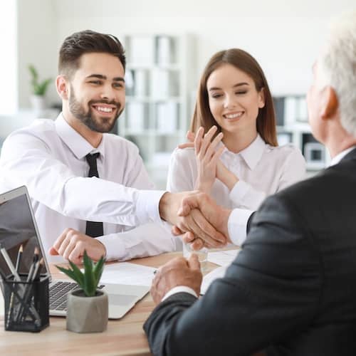 Young couple shaking hands with an agent in an office setting.