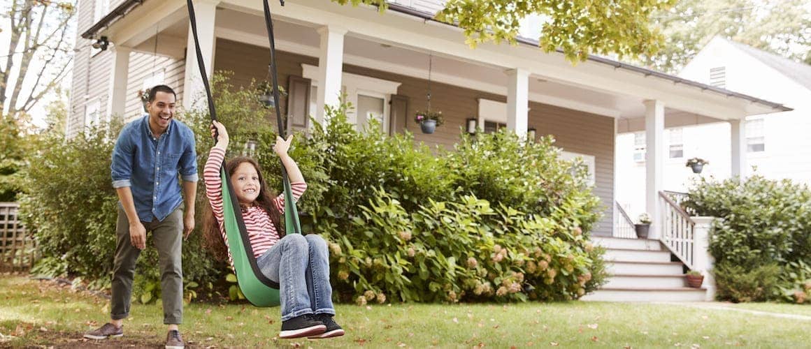 A father swinging his daughter in front yard of a house.