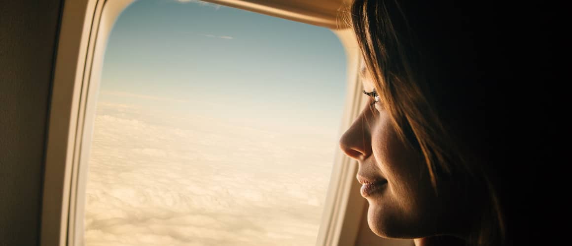 Woman looking out window of airplane with serene look on her face.