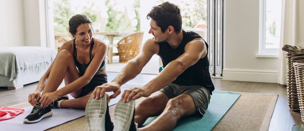 Young couple exercising and stretching together at home on yoga mats.