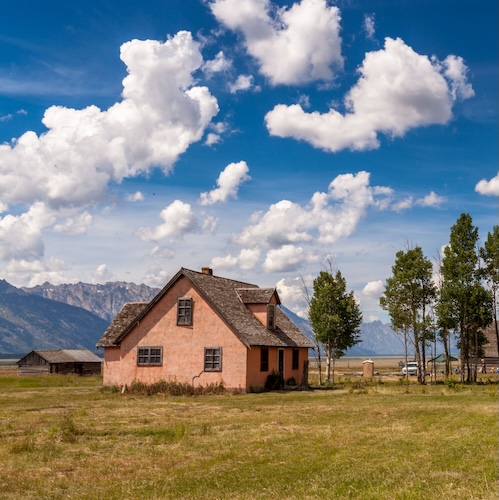 Large brick house on the plains of Wyoming with a few clouds in the bright sky.